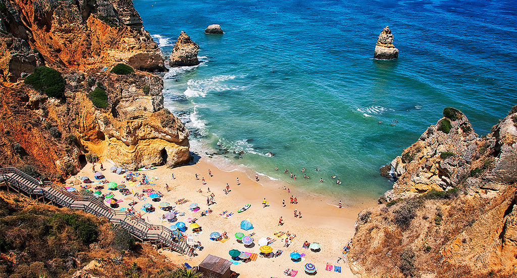 View from a cliff , people on the beach with colourful umbrellas in Lagos Camilo Beach Portugal mischa blog