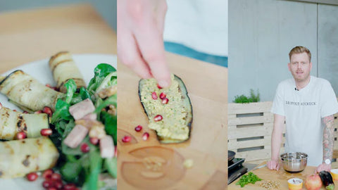 Teller mit gegrillten Auberginenrollen auf Salat, bestreut mit Granatapfelkernen, in einem hellen Raum.