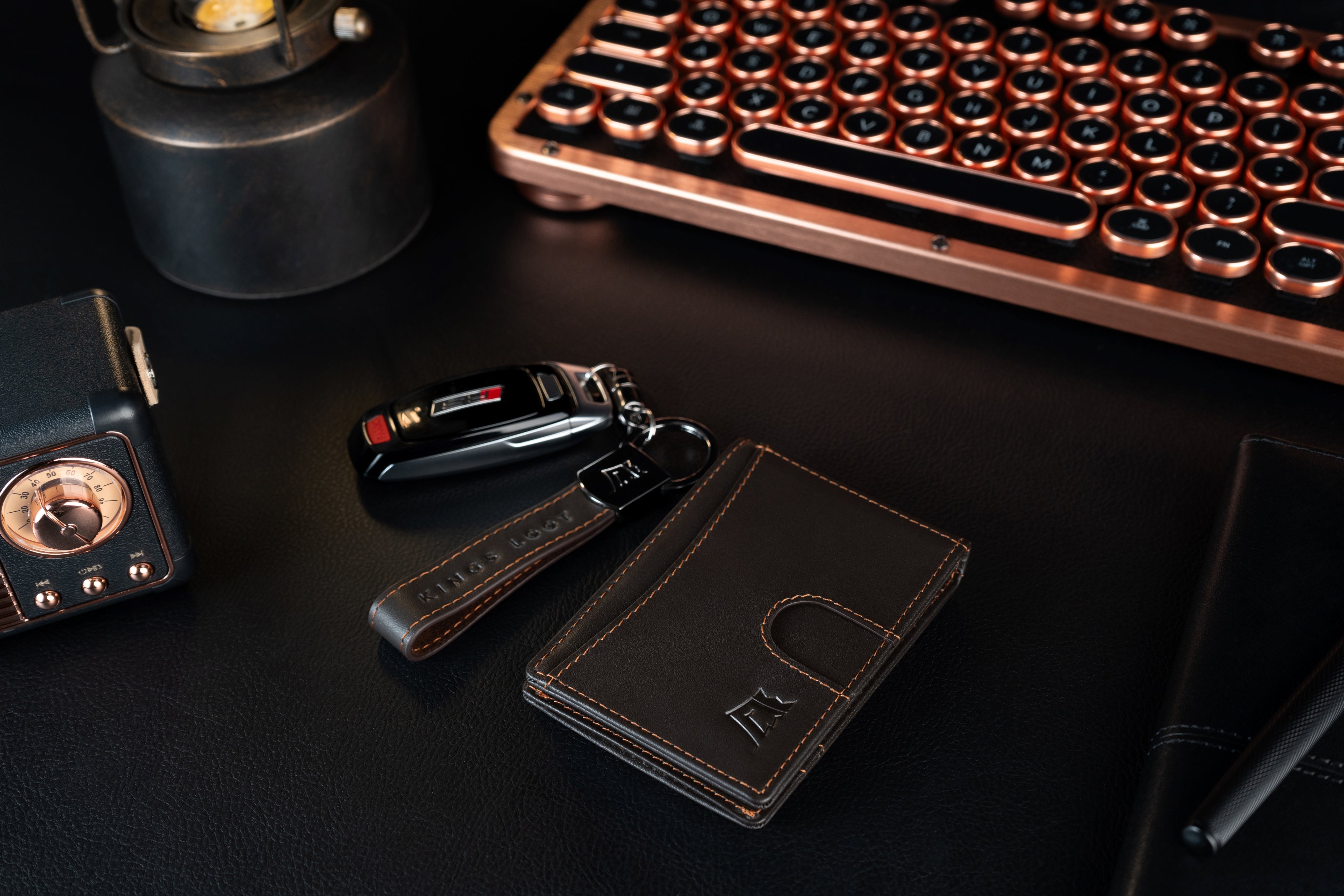 Elegant everyday items including a typewriter keyboard, wallet, lighter, car keys, and a notebook on a dark surface.