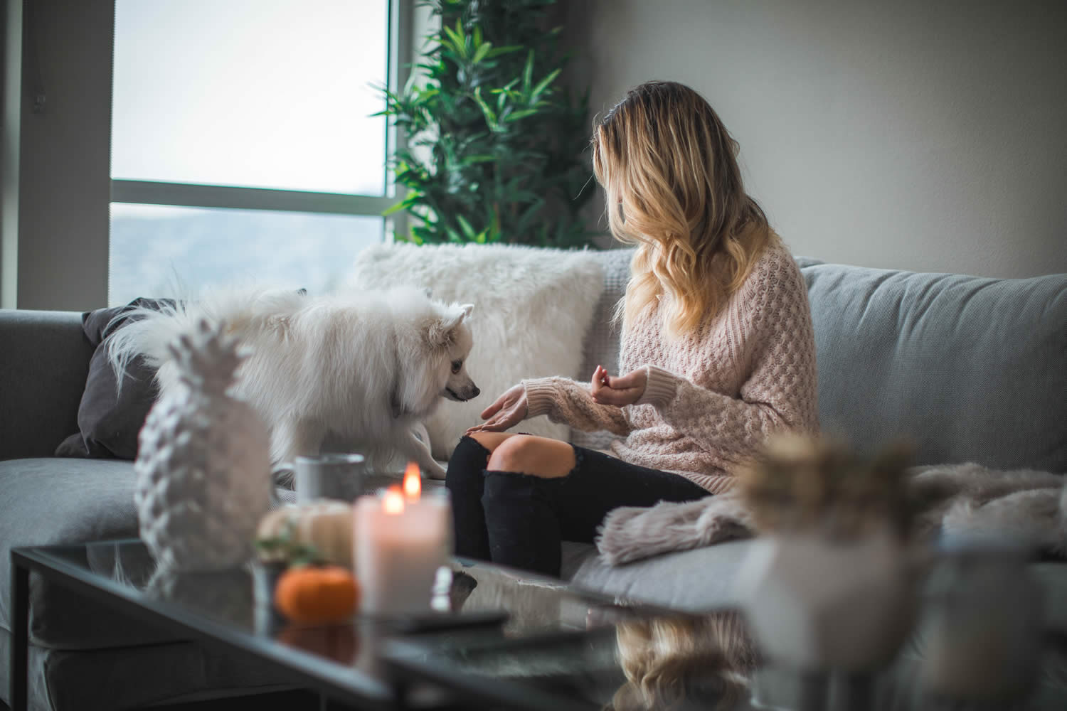 A woman sitting on a sofa with her dog and candles on the table