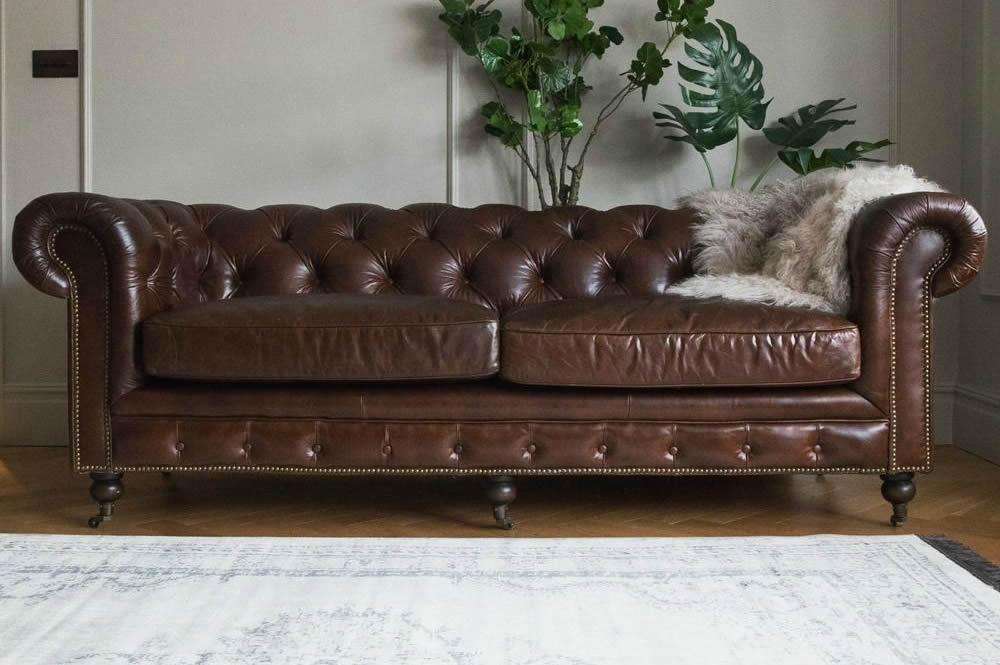 Dark brown Chesterfield leather sofa with grey throw and a light rug 