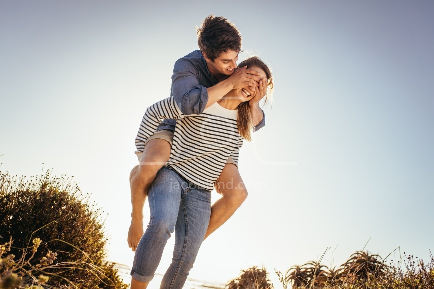 Happy woman carrying her boyfriend on her back on the beach on a sunny day....