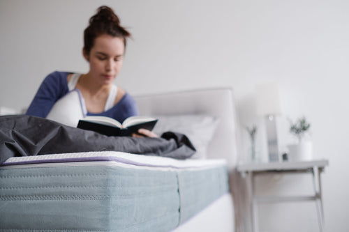 Eine Frau macht es sich mit einem Buch auf der Matratze gemütlich