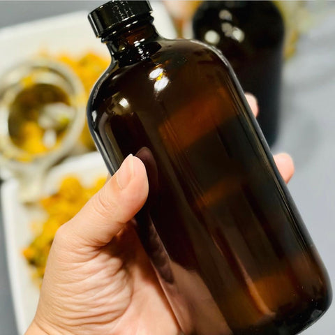 a hand holding a brown glass bottle of calendula oil