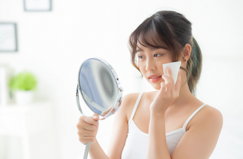 asian woman looking into mirror skincare