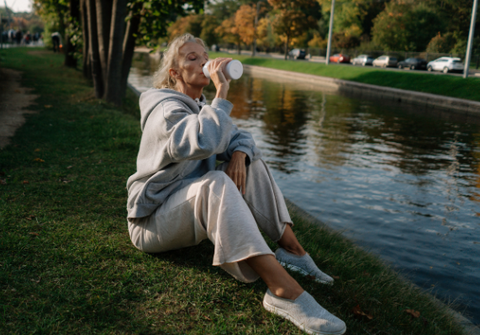 woman drinking water and sitting next to lake