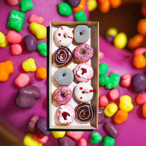 10 Halloween themed donuts in a box one a background of a close up of one of the purple donuts covered in Nerds candy.