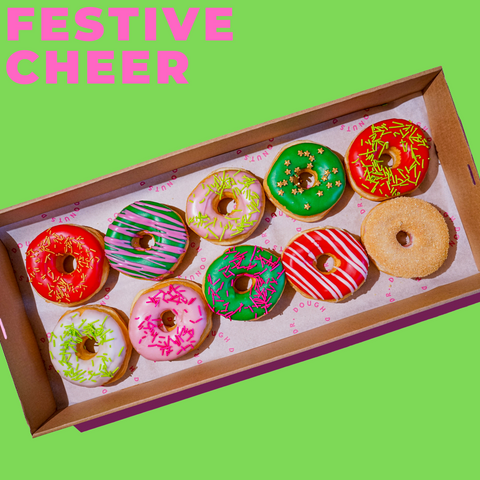 This images features 10 festive cheer donuts in a box. Each donut is decorates in green, red and gold glazes and toppings to help spread the festive spirit and cheer.