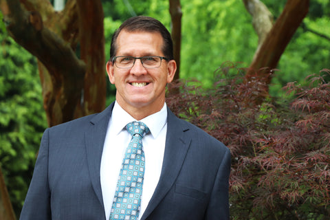 Man in suit with obscured face, standing outdoors amidst greenery