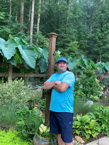 Mike standing in a serene garden, holding a wooden post