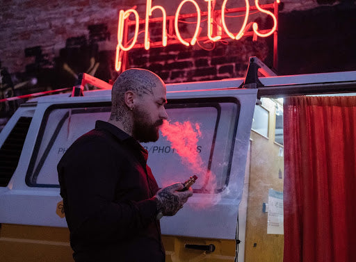 A tattooed man with a shaved head vaping