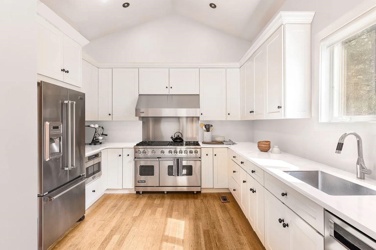White shaker kitchen with stainless steel luxury appliances- wolf, subzero with black decorative hardware.