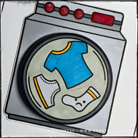 An angled up close view of the drum of the washing machine on this handmade card. A tiny pair of underroos along with a t-shirt and sock are floating in the washing machine. Propelled by a small plastic spring that lays flat when mailing the card, the circle die-cut wiggles back and forth as a fun detail. 