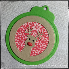 A green holiday tag with an inlaid design of a reindeer - most likely Rudolph. The inner background has the pattern of a sweater in shades of white and red. The reindeer's nose is red and slightly dimensional as it's made from fun foam. 