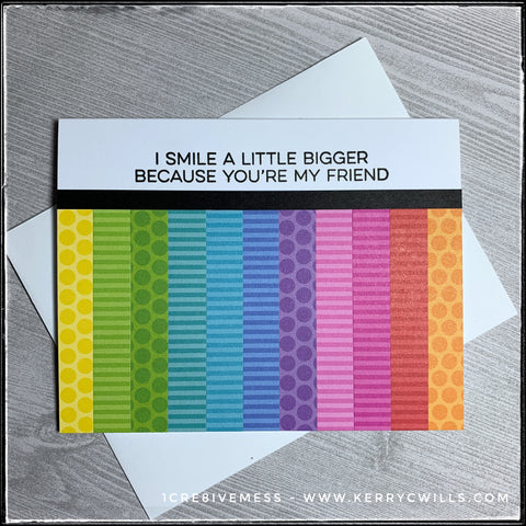 Using a sketch as inspiration, I combined a rainbow of colors in a variety of patterned papers to fill the lower portion of the card front. A happy sentiment is stamped in black ink above a black horizontal strip of cardstock and reads "I smile a little bigger because you're my friend." It includes a plain white envelope and is sure to share some happiness. 