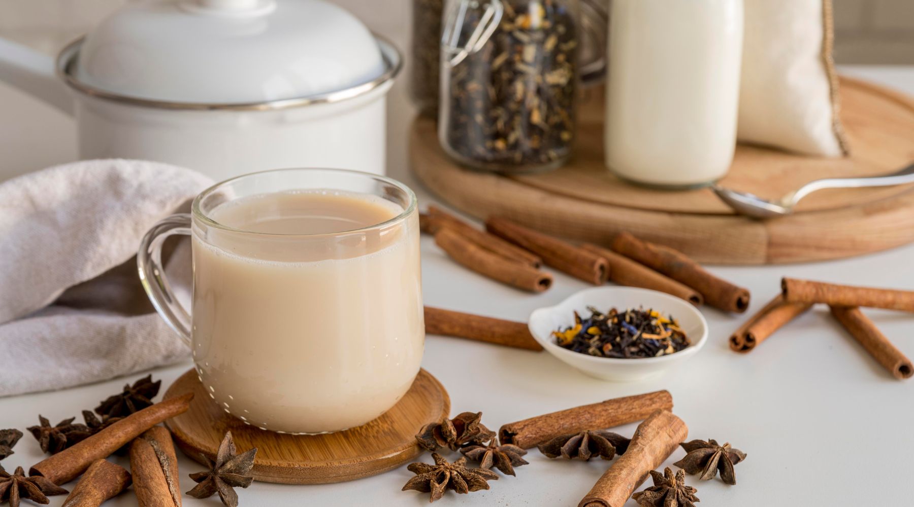 Collombatti Naturals 8 reasons to love chai this winter blog -  A mug of chai in a clear glass mug on a wooden coaster with chai spices scattered around the mug