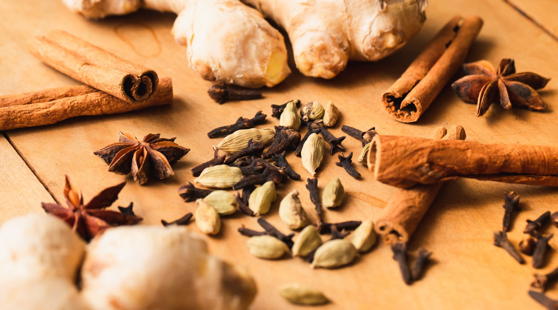 Collombatti Naturals 8 reasons to love chai this winter blog - chai spices, giver, cloves, star anise, cinnamon and cardamom scattered all over a wooden background