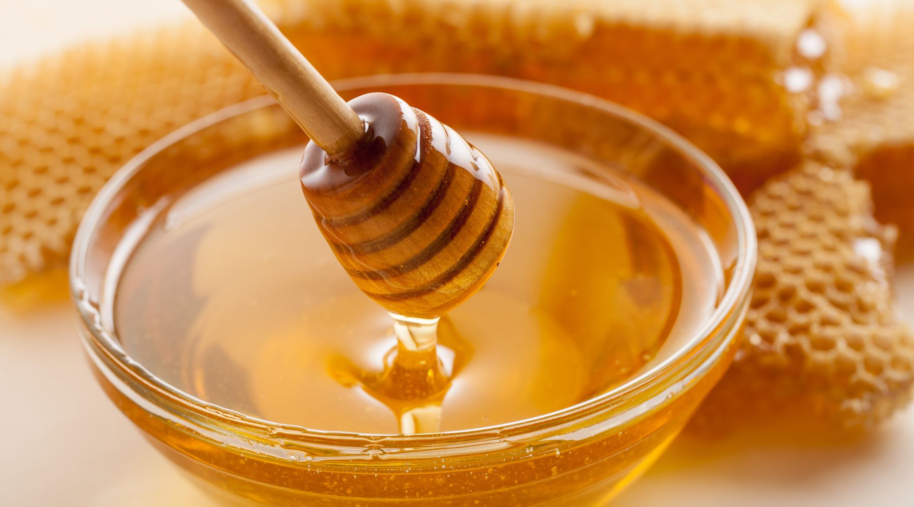 Collombatti Naturals Interesting Facts About Bees You Need To Know Blog - a glass bowl of honey with a wooden honey dipper surrounded by honeycomb