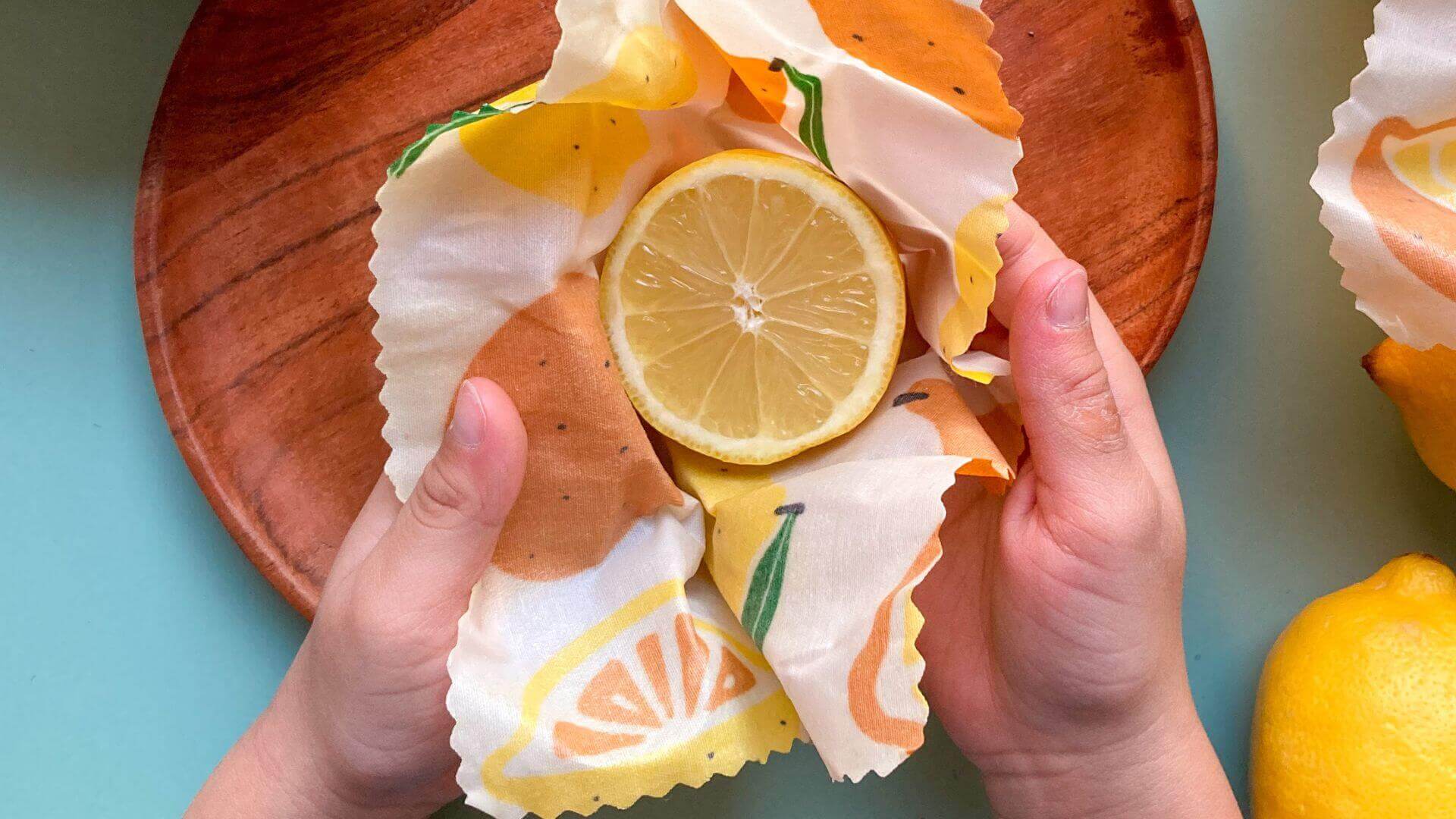 Collombatti Naturals Beeswax Wraps FAQ picture of someone wrapping a cut lemon in a beeswax wrap