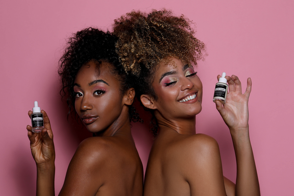 two women against bright pink background holding skincare products