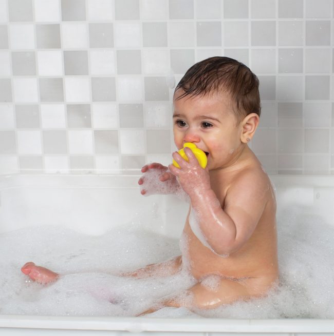 A baby boy on the bath tub playing with Playgro yellow color Rubber duckie in his mouth