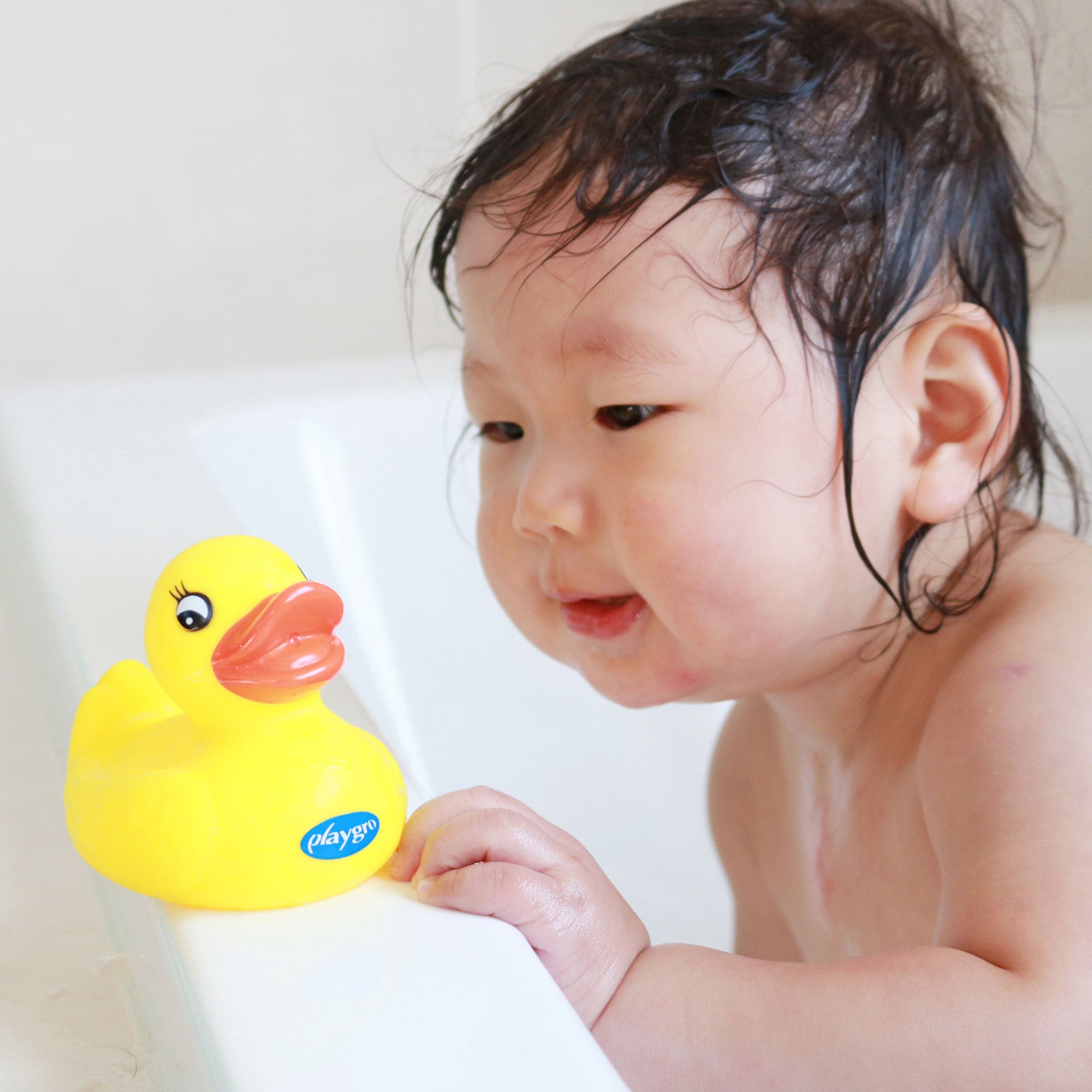 A toddler girl is playing a rubber duckie at the bath tub