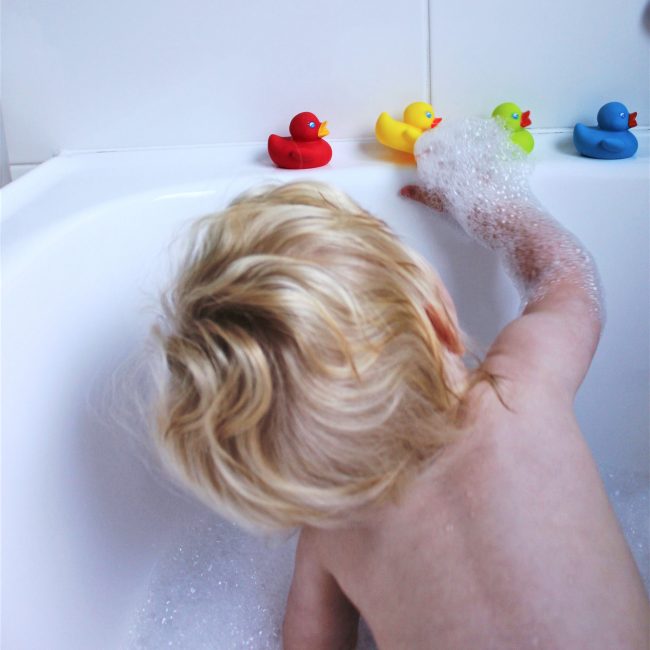 A toddler boy on the bubble buth tub is reaching out to Playgro colorful rubber duckie