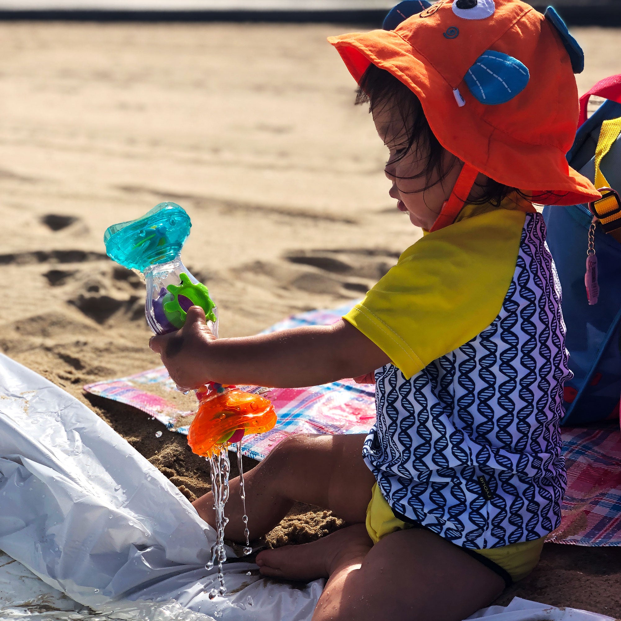 a toddler girl in the beach is playing with Playgro Rainmaker toys