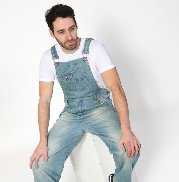 Seated wearing pale wash Uskees denim overalls.