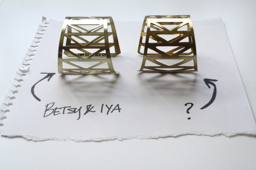 Two geometric cuff bracelets lay side by side, one designed and made by betsy & iya and the other we believe to be a copy of the original design. 