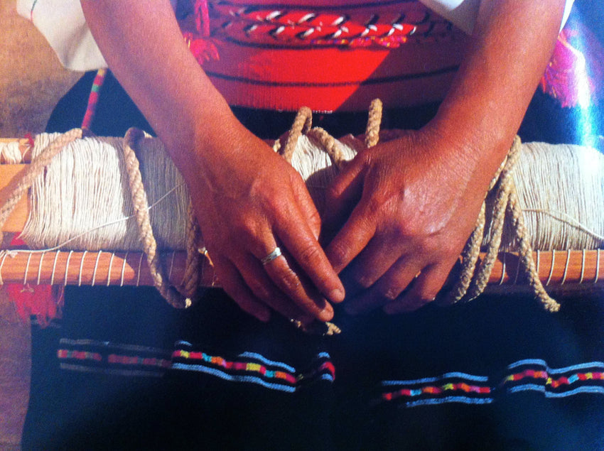 A Mexican weaver's hands lay on top of her colorful dress and weaving project.