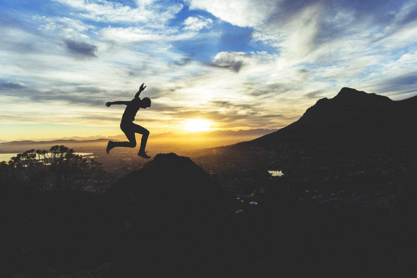 Sunset image of a person taking a big leap off of a cliff.