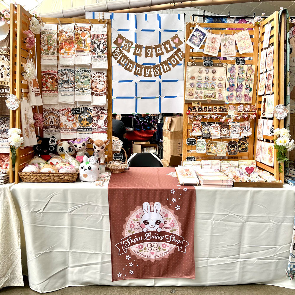 A photo of a table display at a convention featuring Sugar Bunny Shop's merchandise.