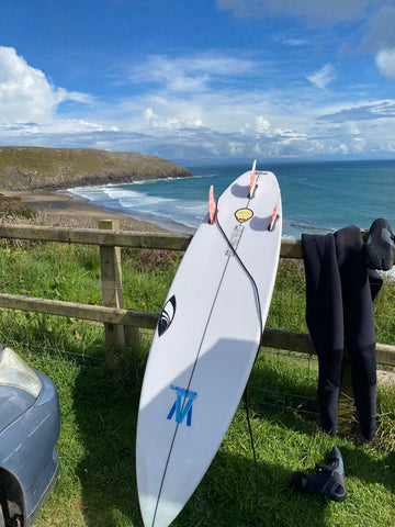 Sharp Eye surfboard with FCS fins and leash overlooking surf beach Porth Ceiriad in North Wales, UK