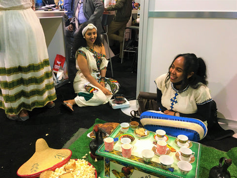 Two Ethiopian women in traditional Ethiopian dress sitting on the floor behind a traditional coffee service.