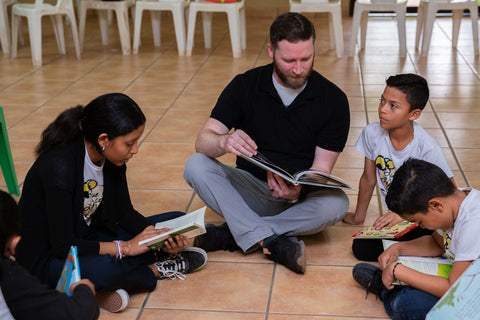 An adult and three children sitting on the ground in a circle and reading