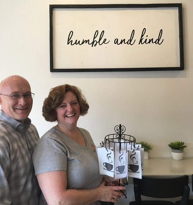 Owners of The Freckled Fox cafe standing in front of sign that reads "Humble and kind"