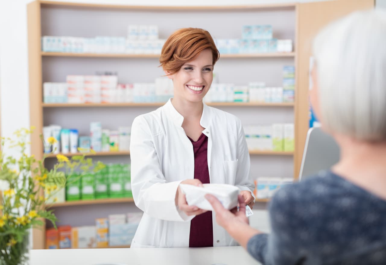 A smiling female pharmacist handing a customer a prescription.