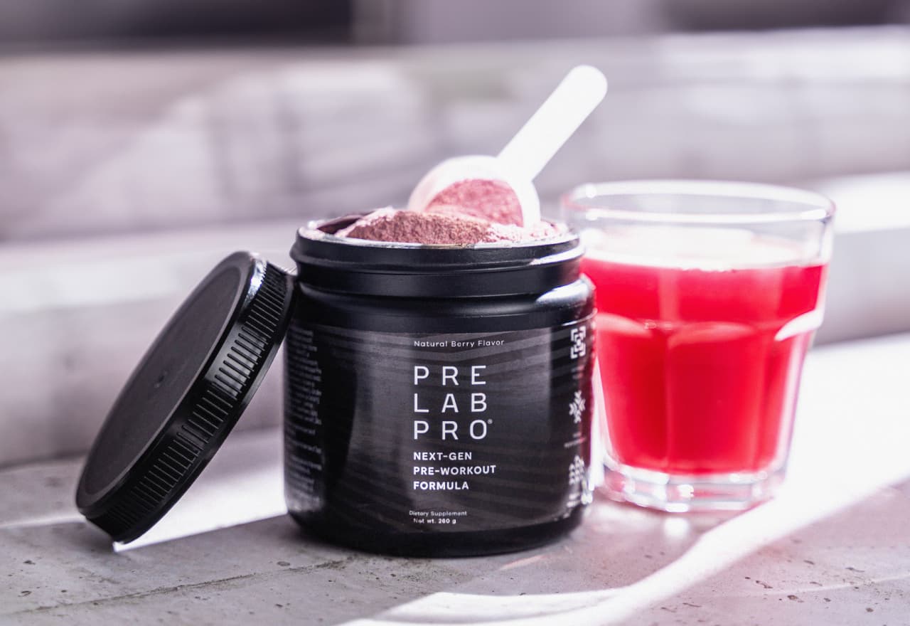 Pre Lab Pro® open tub filled with pink powder next to a glass of pre-workout drink.