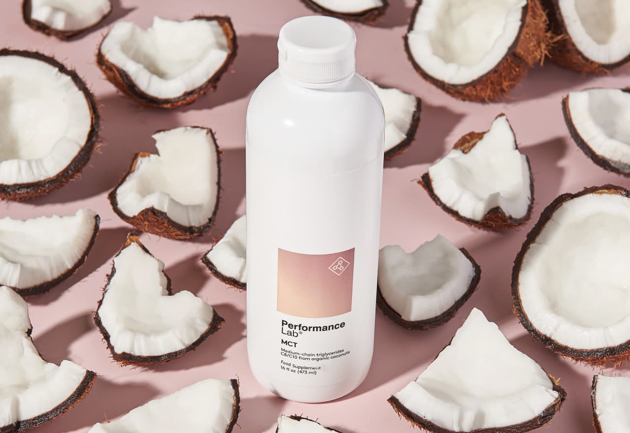 MCT Energy Oil bottle against a pink background surrounded by pieces of raw coconut.