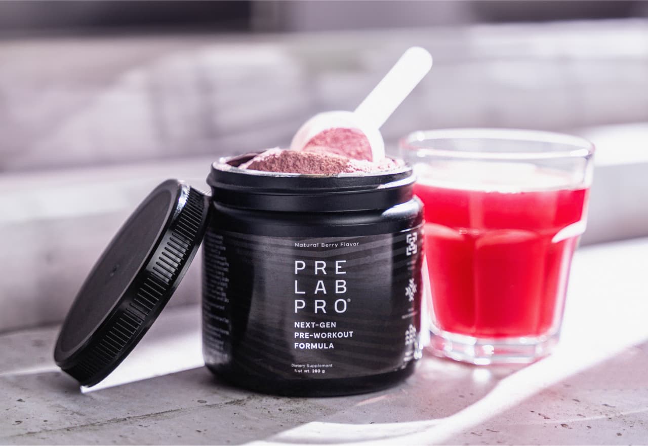Pre Lab Pro® tub filled with pink powder and a scoop placed next to a glass of red pre-workout drink.