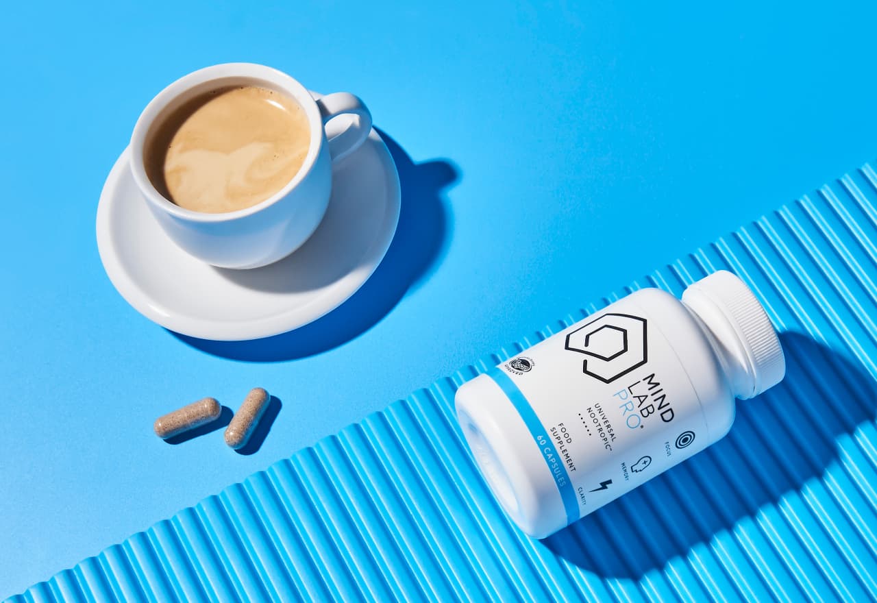 What to take: Nootropics or Coffee? A steaming mug of coffee next to two nootropic capsules.