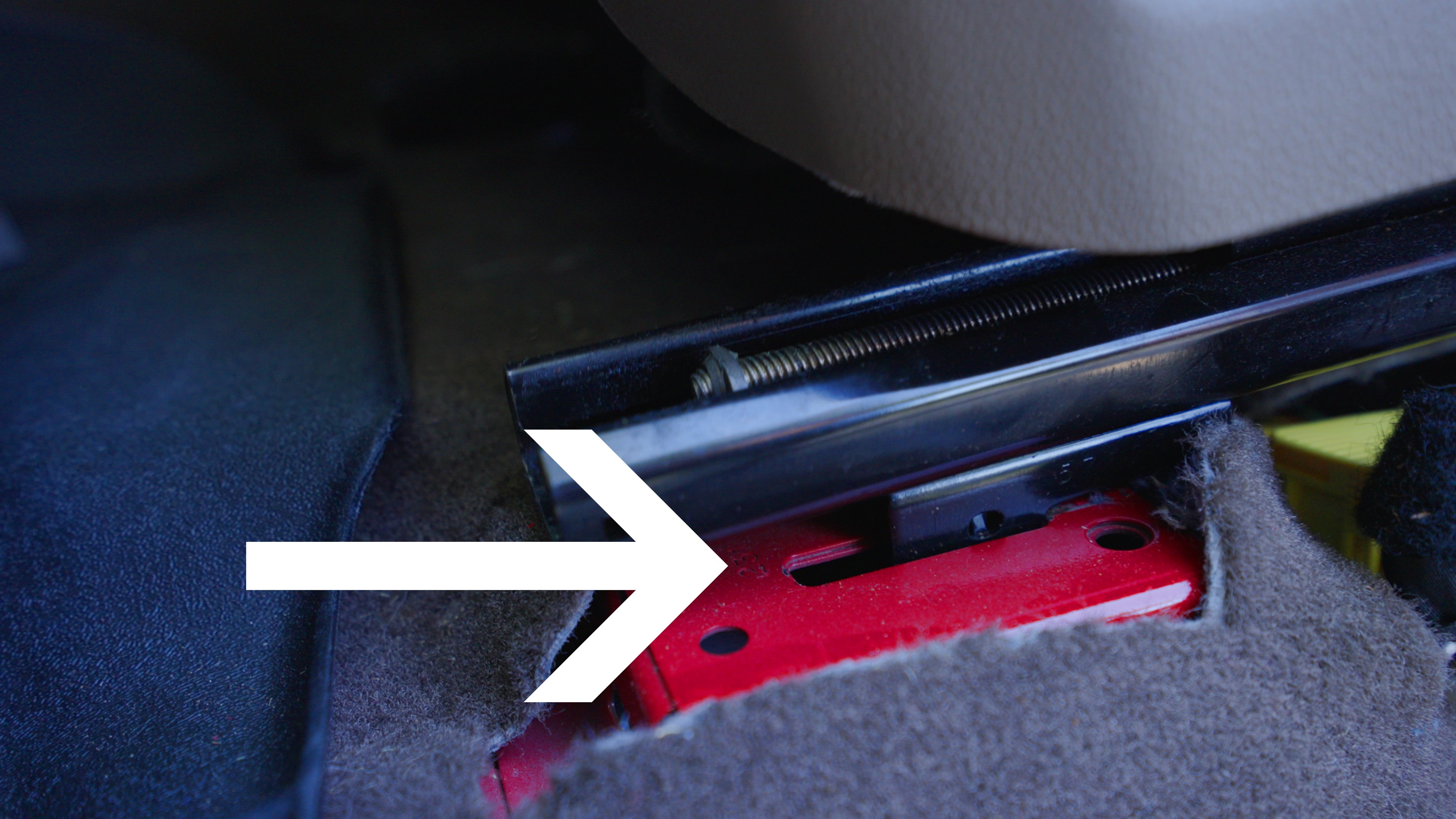 a photo displaying a white arrow pointing to the metal tabs locking a seat frame into a vehicle