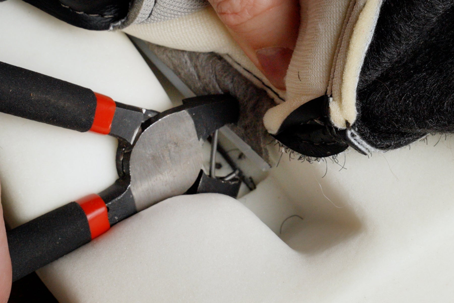 image of someone attaching a hog ring to connect a seat cover to a foam cushion