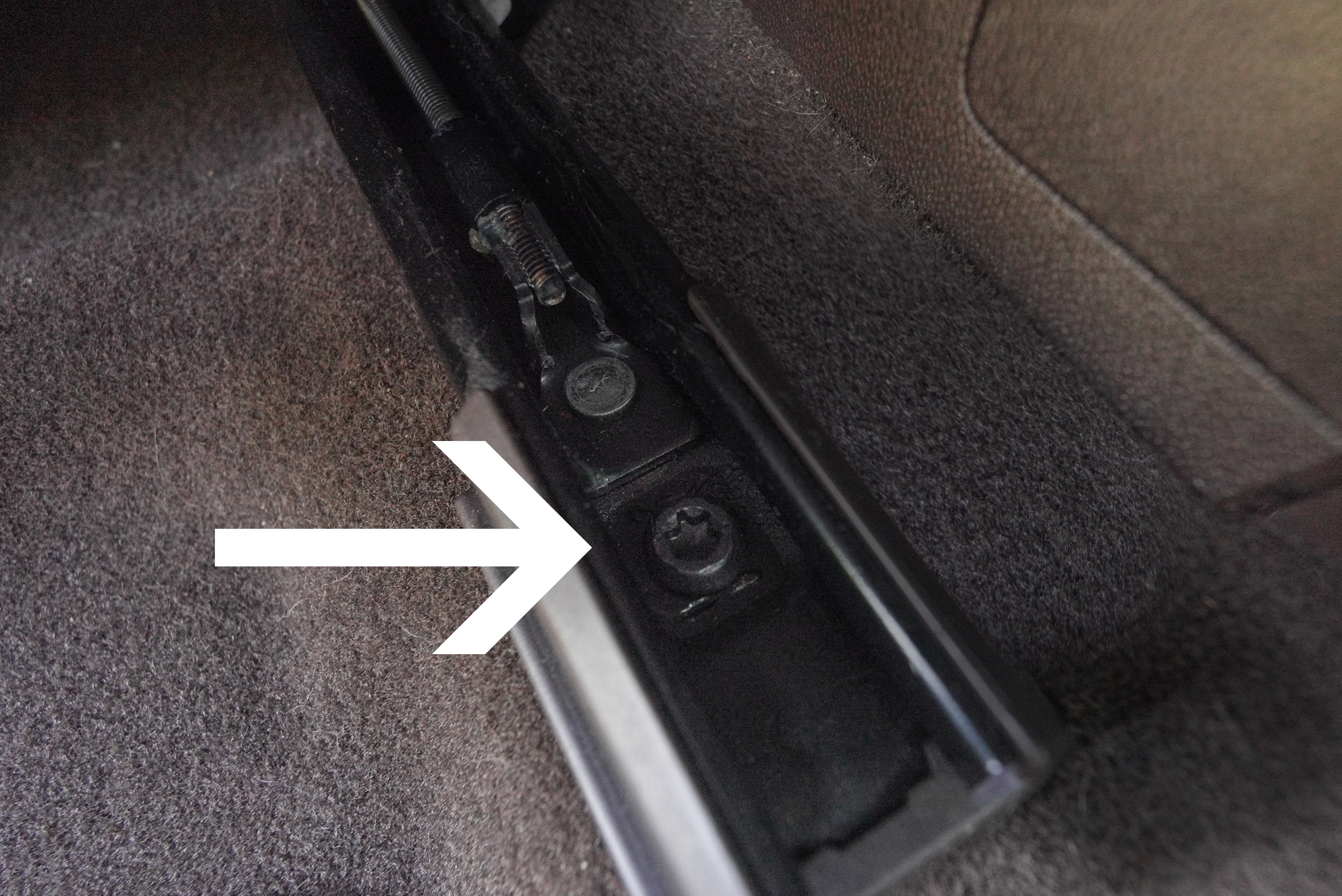 an image with a white arrow pointing to the torx nut recessed within the track of a seat frame, connecting the seat to the vehicle