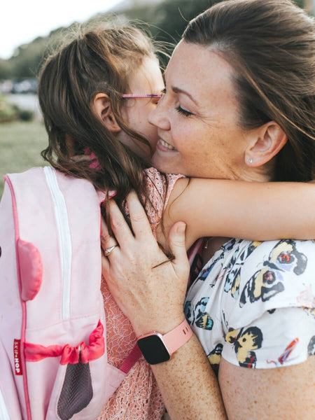 little girl with a pink backpack hugging her mom on the first day of school. They are wearing matching mommy and me always in my heart jewelry from Little Girl's Pearls.