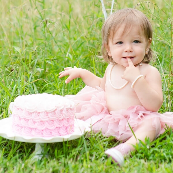 Little girl in pink tutu wearing pearl necklace next to a pink cake