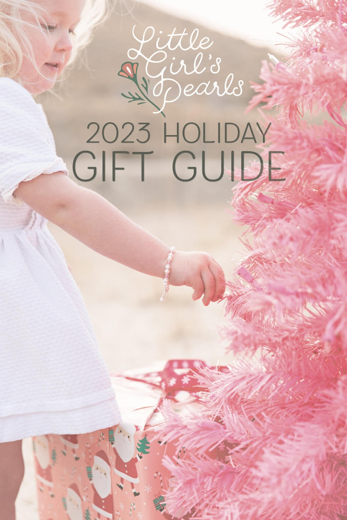 A festive girl near a pink Christmas tree she's wearing a little girl's pearls bracelet.