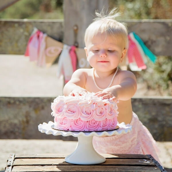 Little girl putting hands in pink cake and wearing pearl necklace