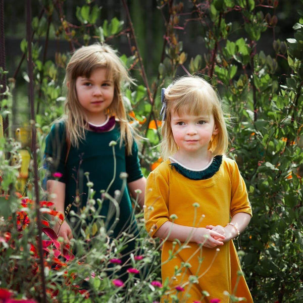 two little girls in Thanksgiving dresses wearing pearl bracelets in the garden.